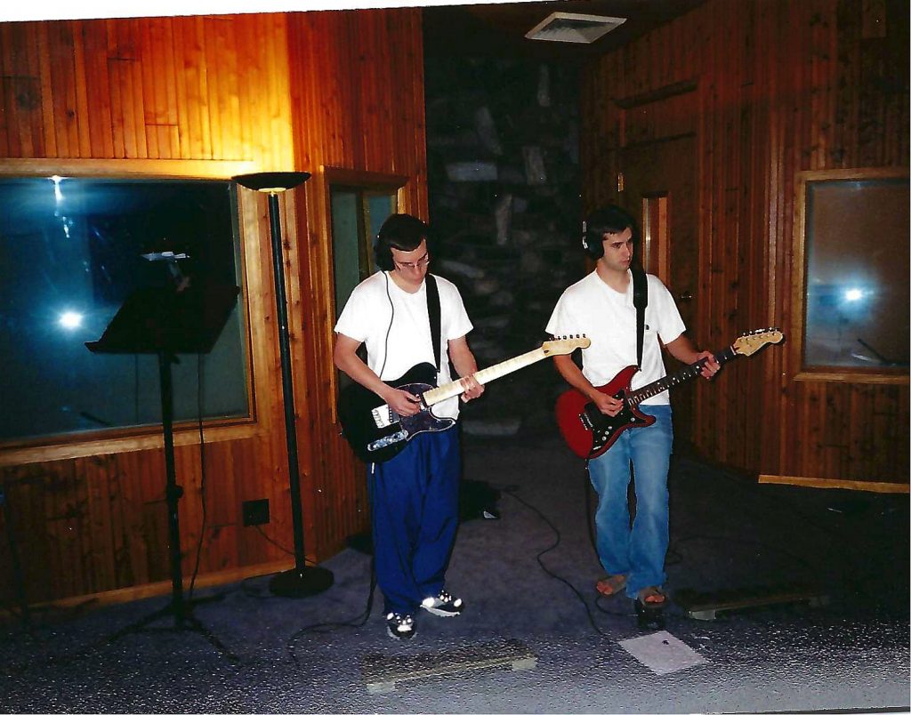 Two musicians wearing headphones playing electric guitars in a wood-paneled studio tracking room at Soundscape Studios, early 2000s.