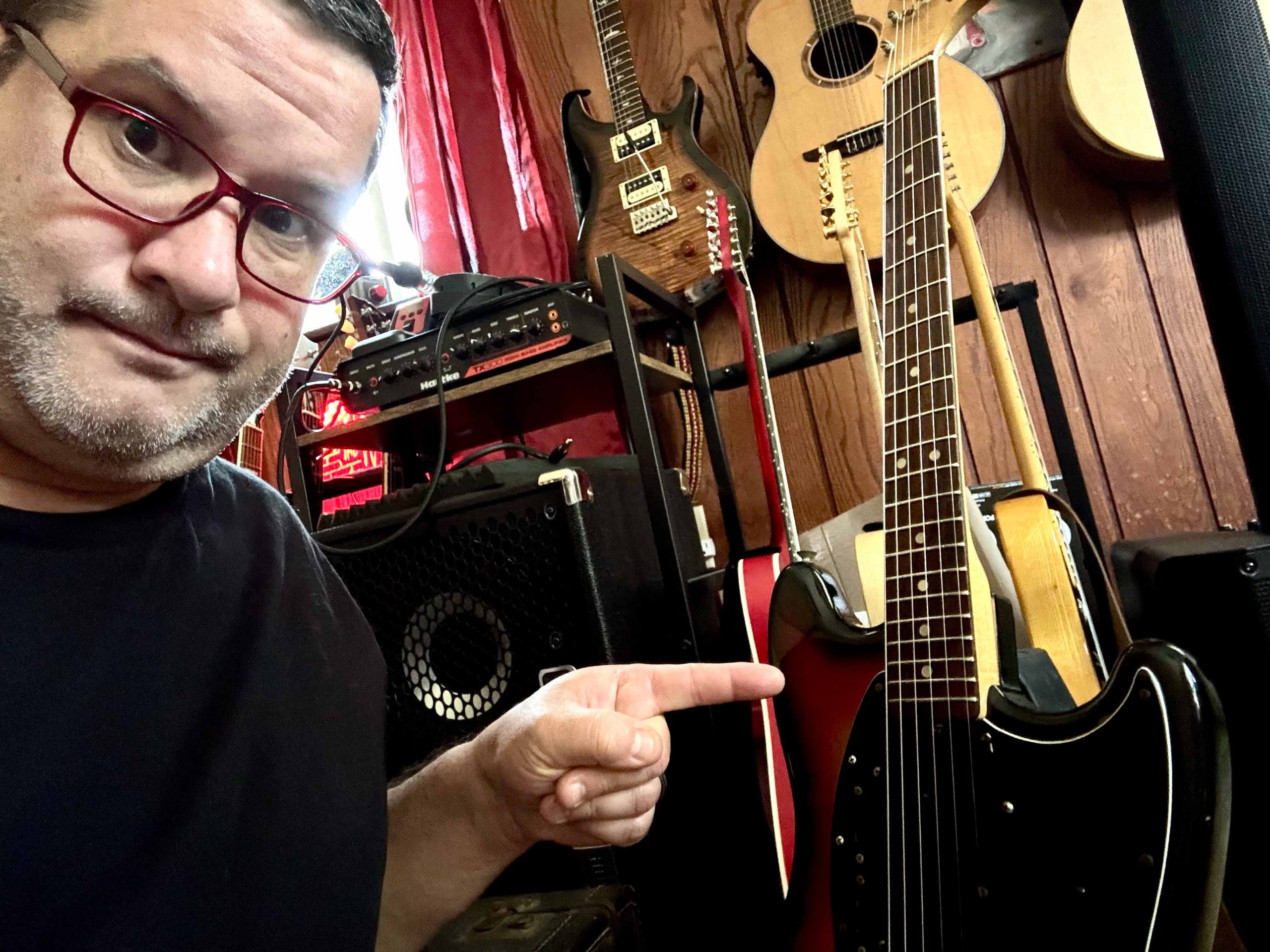 Guitarist with 30+ years of experience pointing at electric guitar in home studio, embracing rhythm playing over shredding.