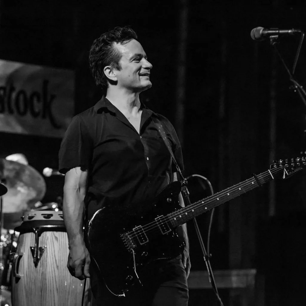 A man with a guitar smiling on stage overlooking the crowd